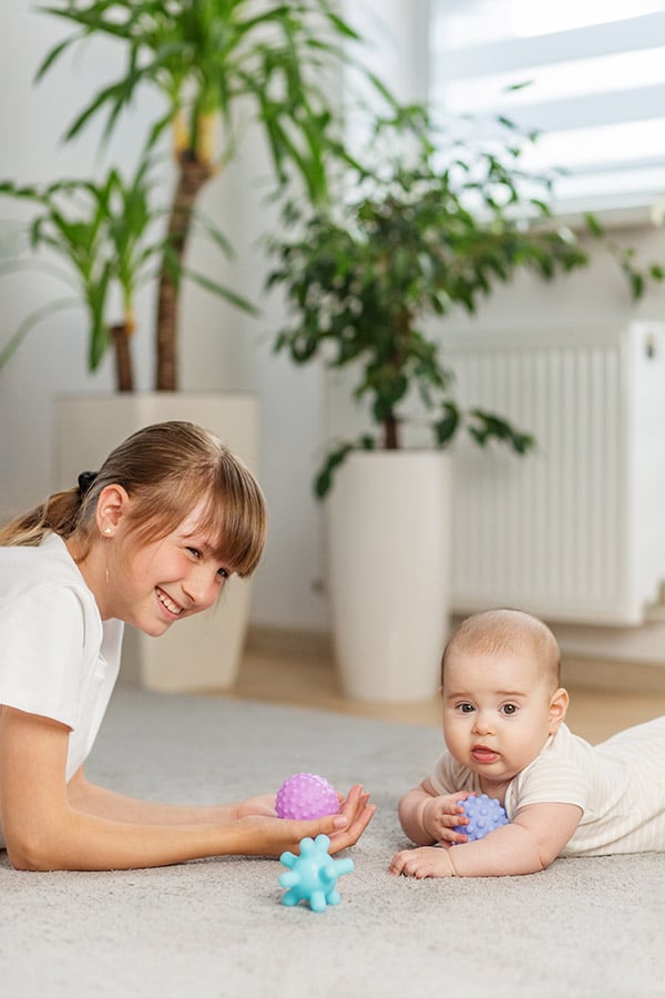 Older Sibling Playing With Baby on Carpet. Tummy time smarterair brother sister playing on clearn rug